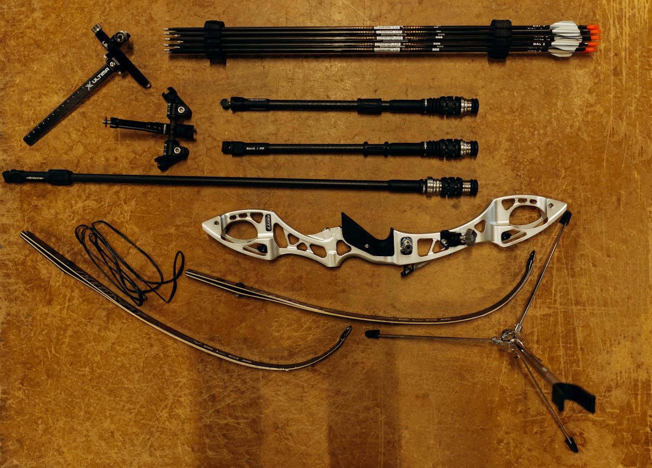 An artistic flat lay of archery equipment featuring a bow, arrows, and accessories on a wooden surface.