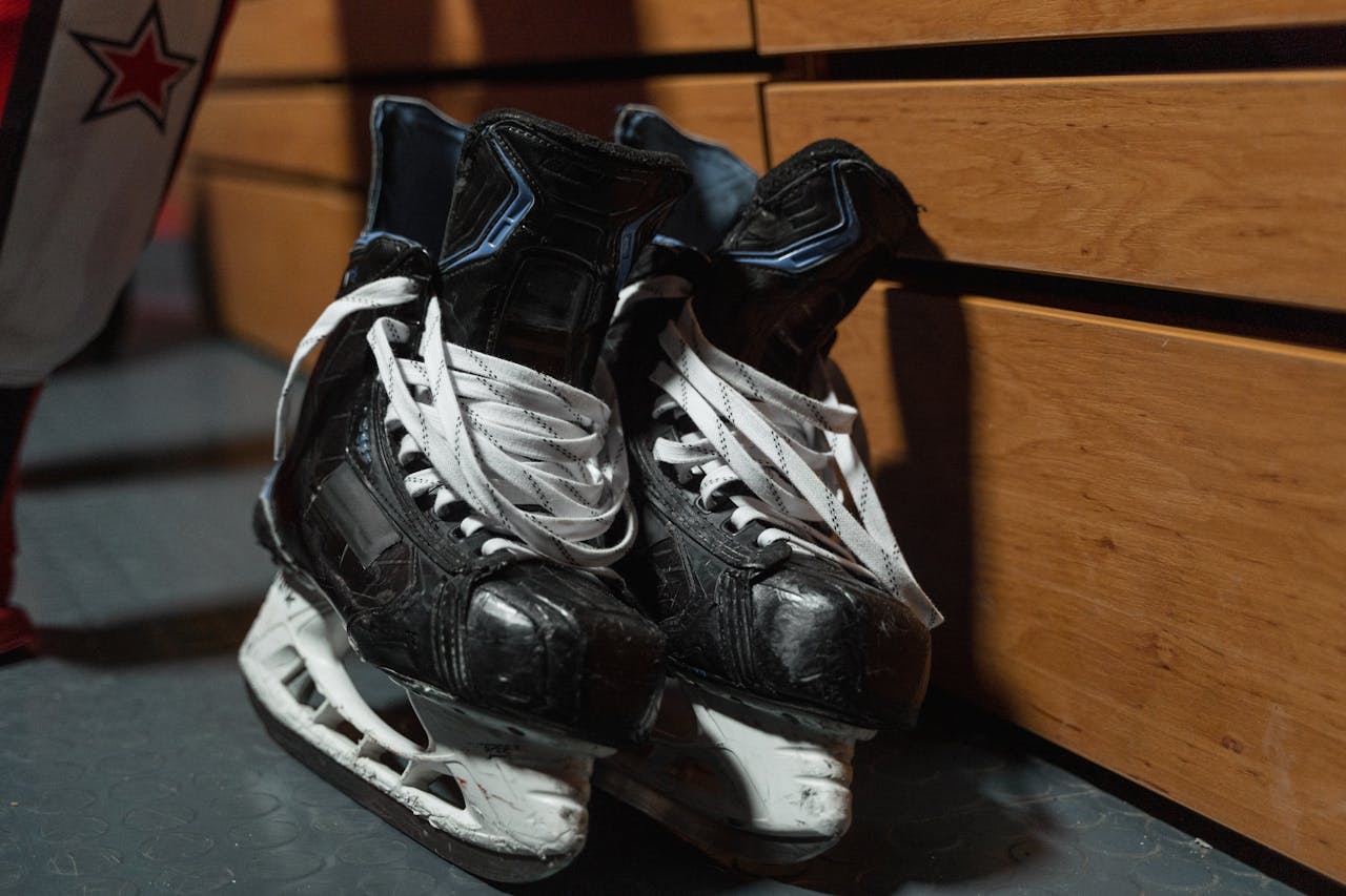 A pair of used ice hockey skates lie on the floor in a locker room, showcasing sports equipment.